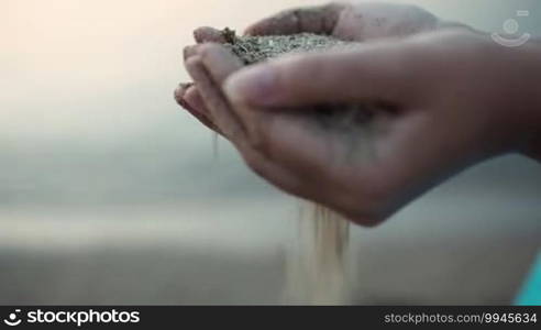 Close up view of sea sand running through a woman's hands against a blurred ocean backdrop with copyspace conceptual of a summer vacation
