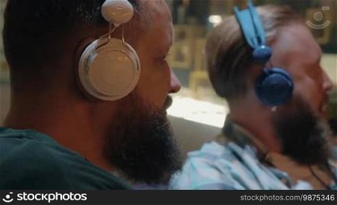 Close up view of two white mature bearded men listening to music using colorful on-ear headsets