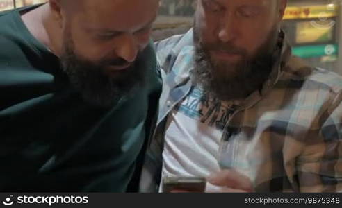 Close up view of two white mature bearded men using smartphone together. Men are relaxing and waiting