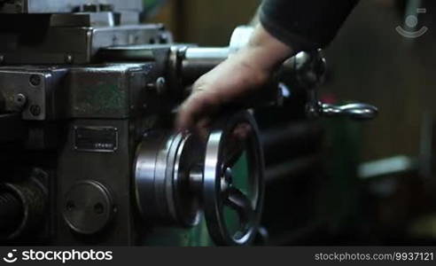 Close up view of worker's hands controlling adjustment wheel and round handle of lathe machine during metal work in workshop