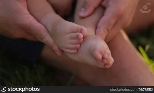 Closeup affectionate father holding tiny infant child's feet in his hands. Caring daddy rubbing small baby boy feet with his hands. Love, tenderness and care concept.
