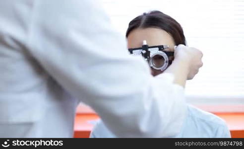 Closeup female optometrist doctor examining eyesight of woman patient in ophthalmology clinic. Experienced optician determining prescription values with trial frame for young attractive woman. Eye care concept.