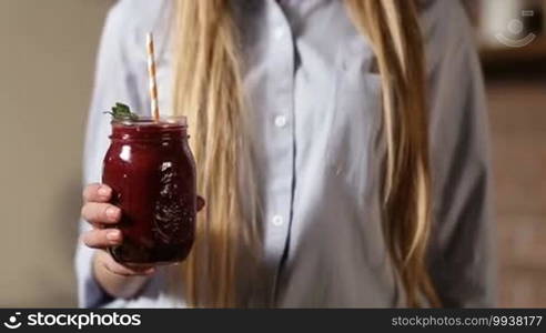 Closeup female with perfect hand holding fresh delicious vegetable smoothie in mason jar. Middle section of woman holding mason jar of fresh beet detox smoothie with striped straw and leaf of mint for decoration. Healthy eating and lifestyle.