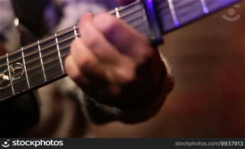 Closeup male hand playing acoustic guitar while rehearsing with the band. Musical instrument with performer hands. Musician playing classic guitar and picking chords.