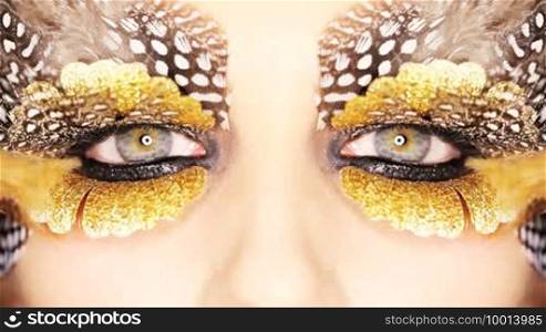 Closeup of a woman's eyes with striking creative makeup of gold and spotted feathers in a beauty and fashion concept.