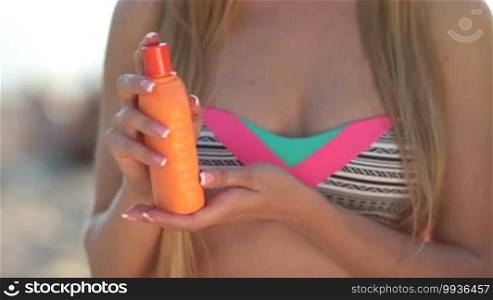 Closeup of a young pretty woman holding an orange tube with sunscreen lotion and applying cream to her hand. The beautiful blonde female is applying sunscreen to her legs and smiling.
