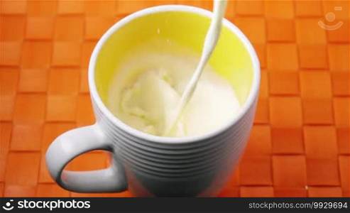 Closeup of cup being filled with milk for breakfast. High angle view of liquid splashing on orange background. Slow motion 250p