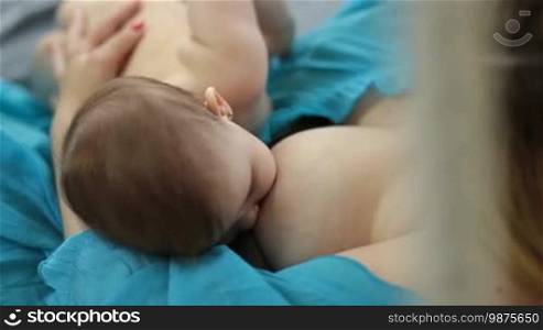 Closeup of infant child sucking mom's breast. Top angle view. Caring mother breastfeeding newborn child at home. Young mother holding her little baby girl and breastfeeding.