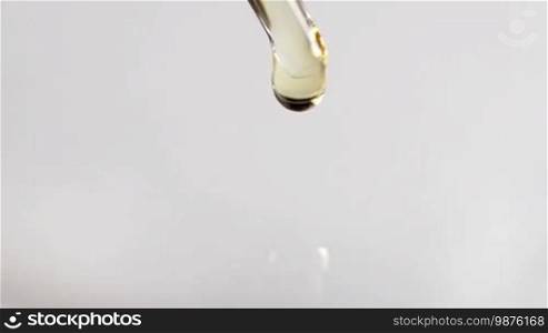 Closeup of liquid oil drop from laboratory pipette to the water over white background