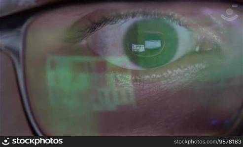 Closeup of man's eye in glasses works on laptop at night. Macro young man in glasses surfing on Internet