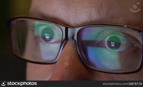 Closeup of man's eyes in glasses works on laptop at night. Macro young man in glasses surfing on Internet