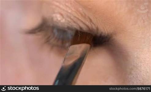 Closeup of woman's eye applying eyeliner. Woman smudging eye pencil with small brush