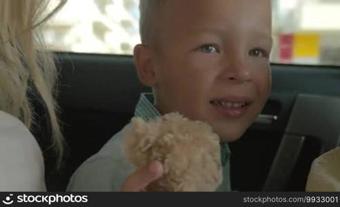 Closeup shot of a boy sitting on the back seat of the car and holding plush toy teddy bear in hands