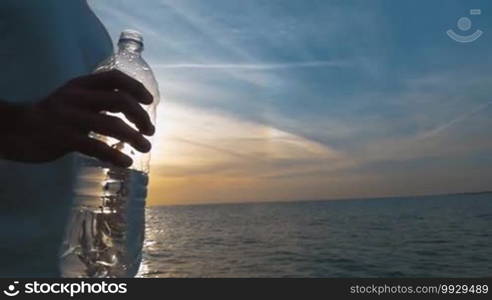 Closeup shot of a plastic water bottle in a male hand. Setting sun is in the background.