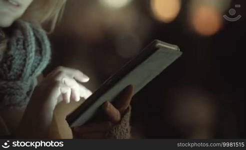 Closeup shot of female hands holding a tablet PC and typing a message. People traffic is in the background.