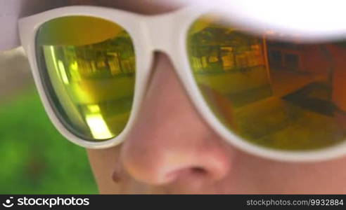 Closeup shot of sunglasses with yellow lenses and a white frame on the face.