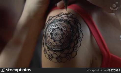 Closeup video of henna tattoo artist drawing on woman's shoulder - video in slow motion