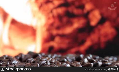 Coffee grains fall on table surface. Background fireplace fire.