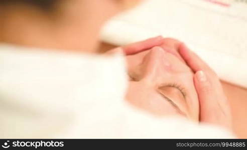 Cosmetician providing facial treatment with a massage. High angle view from the therapist's shoulder