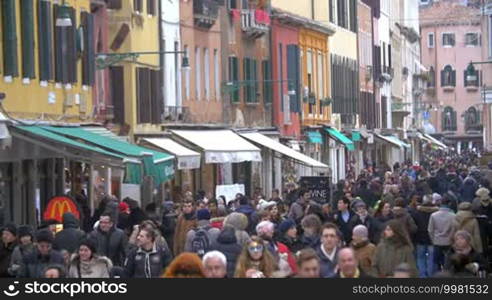 Crowd of people in the street of old Italian city. People passing by vintage buildings with stores and cafes