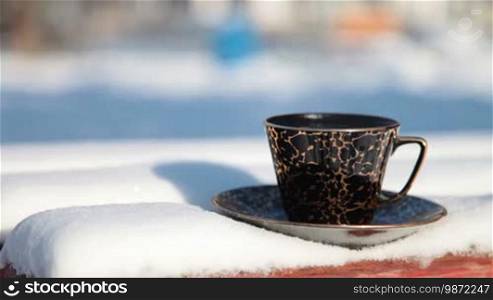 Cup of hot coffee on a snowy bench in winter