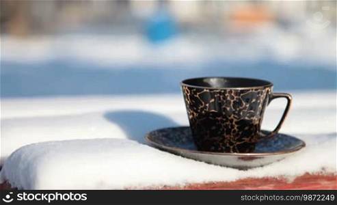Cup of hot coffee on a snowy bench in winter
