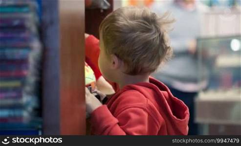 Cute little boy shopping for toys standing at a display rack at a store searching through colorful merchandise