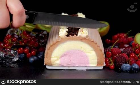 Cutting chocolate vanilla strawberry ice cream roll with berries fruits. Closeup