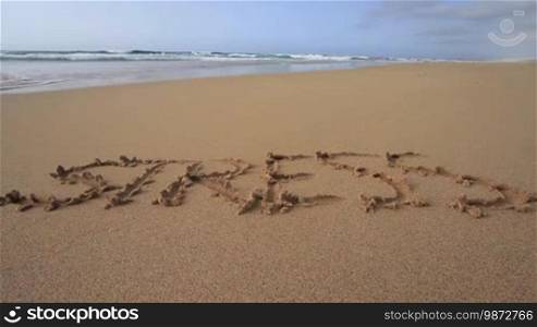 Das Wort "Stress" am Sandstrand in den Sand geschrieben. Es wird vom Meerwasser weggespült.