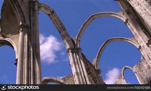 Decorated round arch of stone from an old cathedral; white clouds drift across the blue sky.