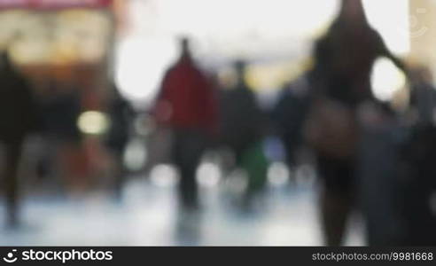 Defocused shot of a crowd of people at the station. They are walking indoors against bright light