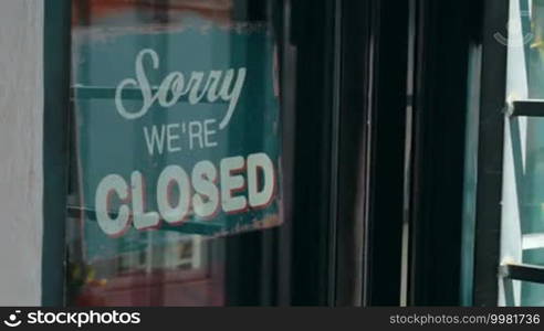 Dolly shot of a woman turning over shop sign. Vintage style open sign inviting customers to come in