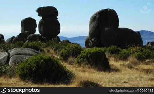 Dunkle runde Steingebilde, runde Steine liegen ubereinander, davor Wiese / Weideland mit kleinen Buschen, im Hintergrund Berglandschaft.
Formatted:
Dark round stone formations, round stones stacked on top of each other, in front meadow/pasture with small bushes, in the background mountain landscape.