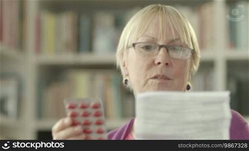 Elderly Caucasian woman with medicine and reading drug prescription. Tilt shot