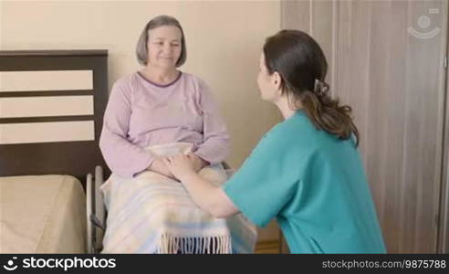 Elderly woman on wheelchair talking with her care assistant. Nursing and caregiving at home or hospice concept.