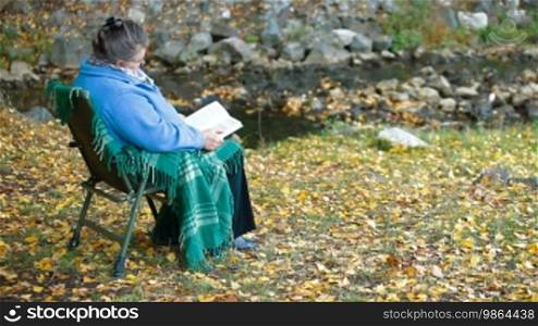 Elderly woman reading a book outdoors - Side View
