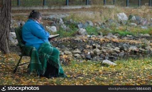 Elderly woman reading a book outdoors - Side View