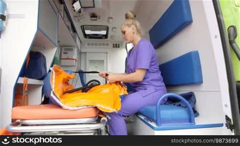 Emergency medical service female paramedic working at the site of illness or injury inside of ambulance preparing inflatable immobilizer and stretcher for patient transportation