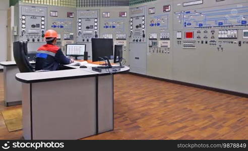 Engineer sits and watching circuits at main control panel of gas compressor station