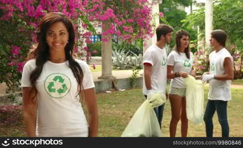 Environment, nature, ecology, clean future. Young people cleaning garbage, happy friends collecting trash on grass, boys and girls picking up plastic bottles in park. Portrait of black woman smiling