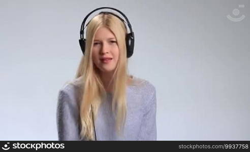 Expressive girl in headphones listening to rhythmic music on the radio over white background. Cheerful young woman enjoying the music, making dance moves and singing along.