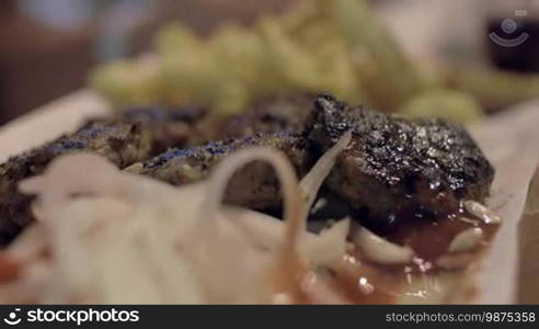 Extreme close-up view of barbecue meat on the plate, that woman's hand waters lemon juice, potatoes, and onion, and then starts to eat