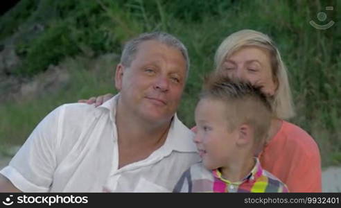 Family looking away. Grandson tickling grandfather's neck while sitting on beach