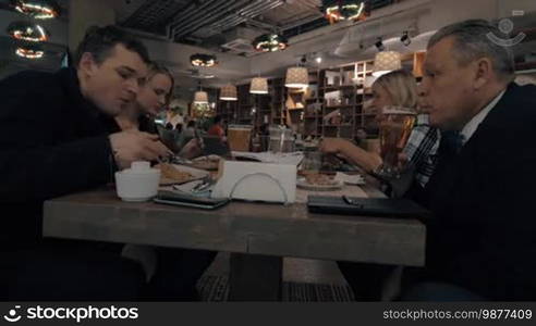 Family of four having dinner in the restaurant. Women enjoying meals while men clanging glasses with beer