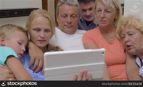 Family of parents, child, and grandparents attracted to the touchpad. They are watching an entertaining video and laughing