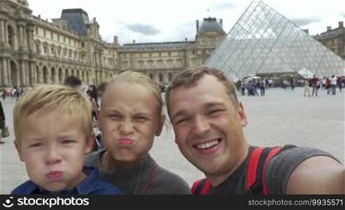 Family of three shooting selfie video near The Louvre museum in Paris. Mother, father, and son laughing and making funny faces