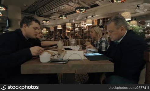 Family spending evening together. They having dinner in the restaurant, senior man working with tablet computer