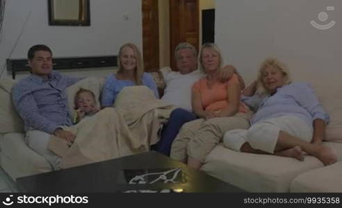 Family spending quiet evening at home. Parents, child, and grandparents sitting on the sofa and watching TV