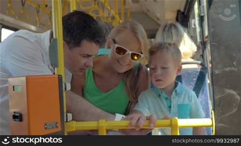 Family with child riding in city bus. Father showing the son how smartwatch works and allows him to use it
