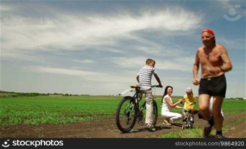 Family with children having a weekend excursion on their bikes, senior man running.